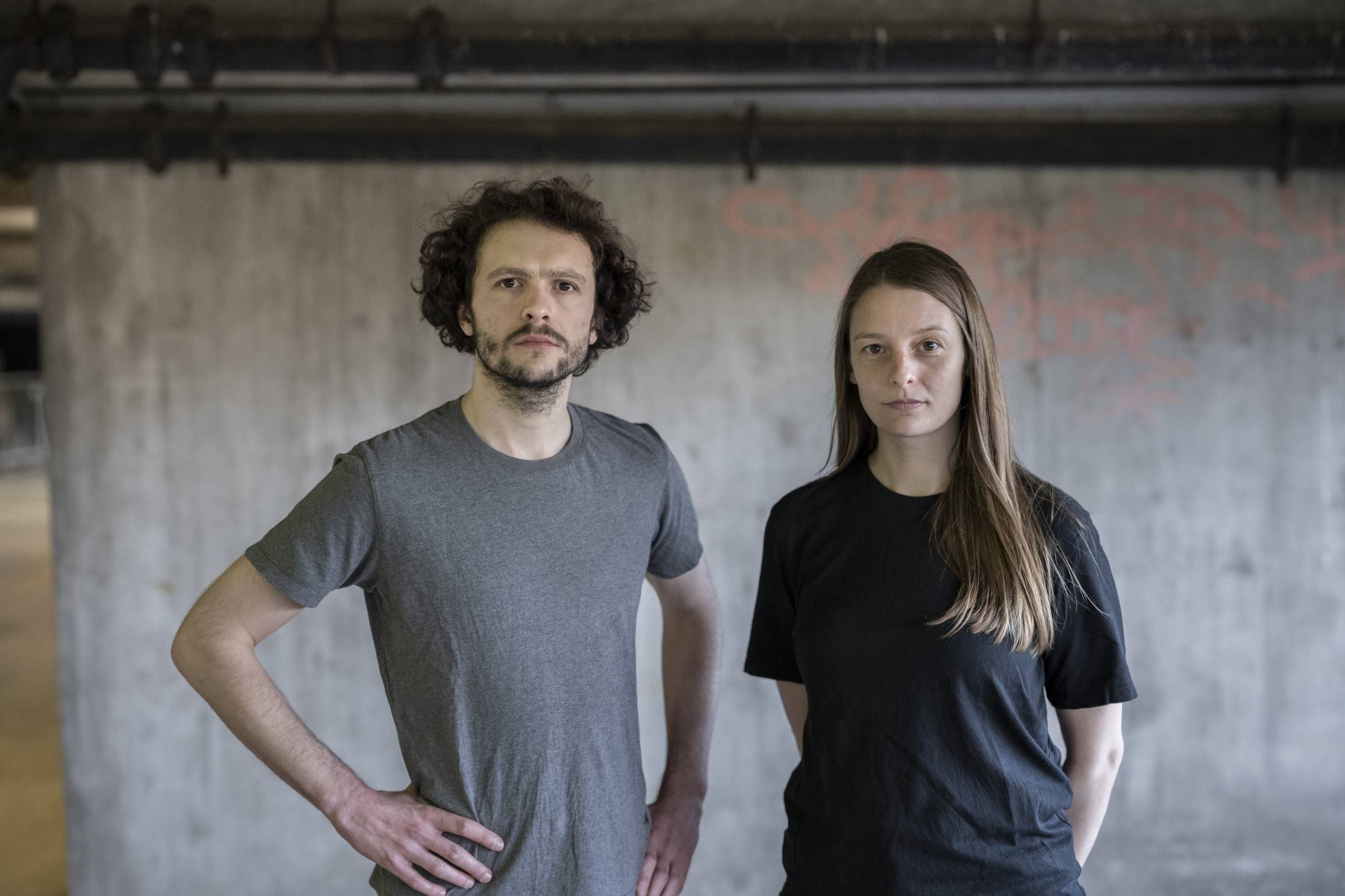 A man and a woman standing in front of a concrete wall.